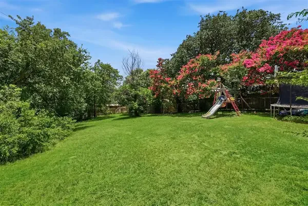 Fenced backyard with mature crepe myrtles and a play set